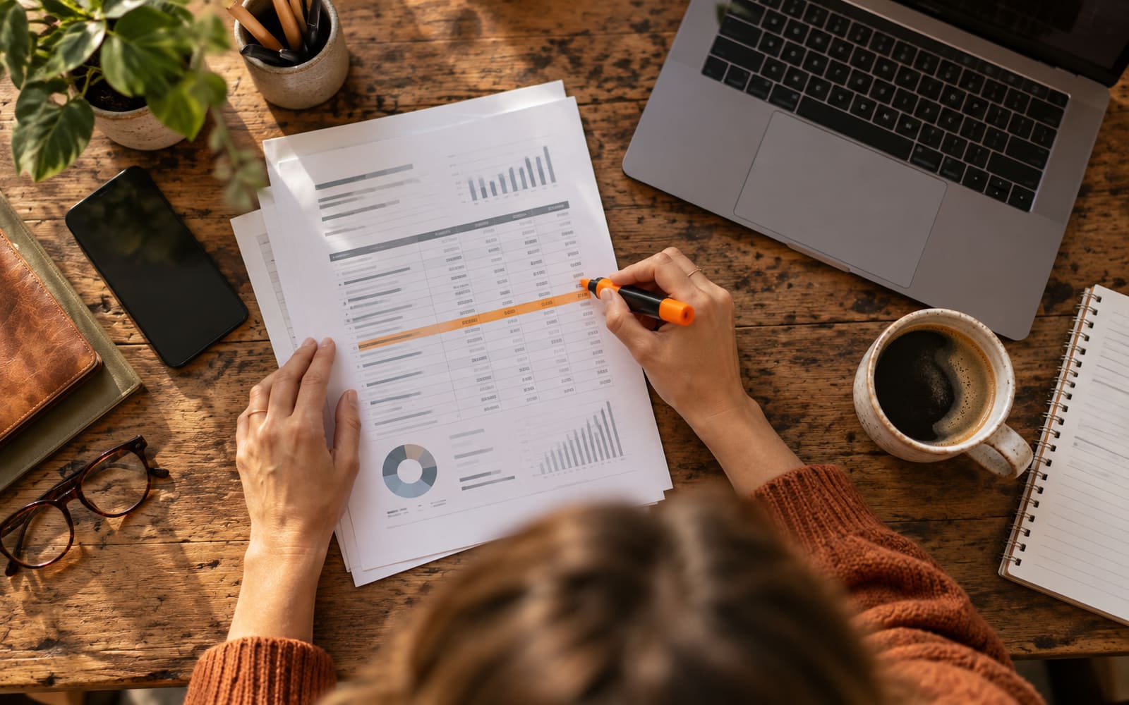 A printed profit and loss report with a highlighted line, seen from above beside a laptop